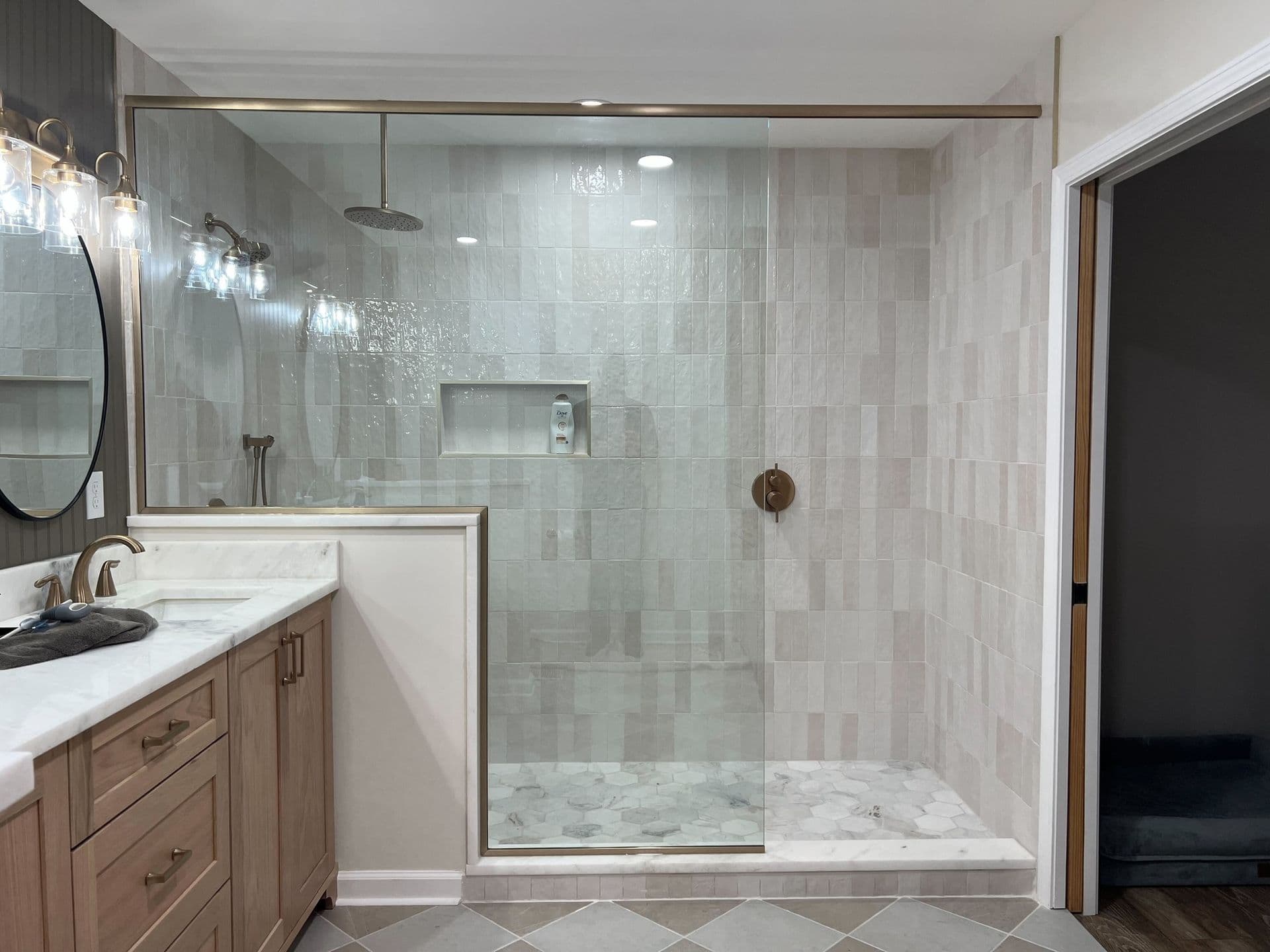 Modern bathroom featuring a glass-enclosed shower with beige tiles, a rain shower head, a built-in niche, and a light wood vanity with dual sinks.