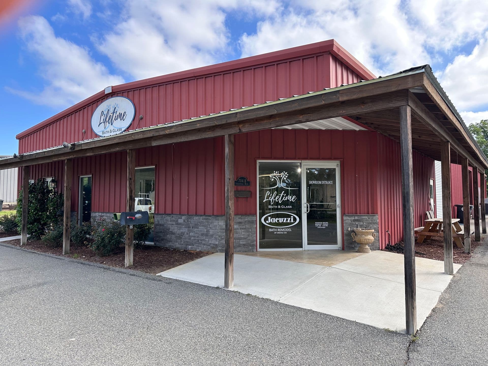 A red metal building with a wooden porch, displaying signs for "Lifetime Gutters" and "Jacuzzi" on the door. The sky is partly cloudy.