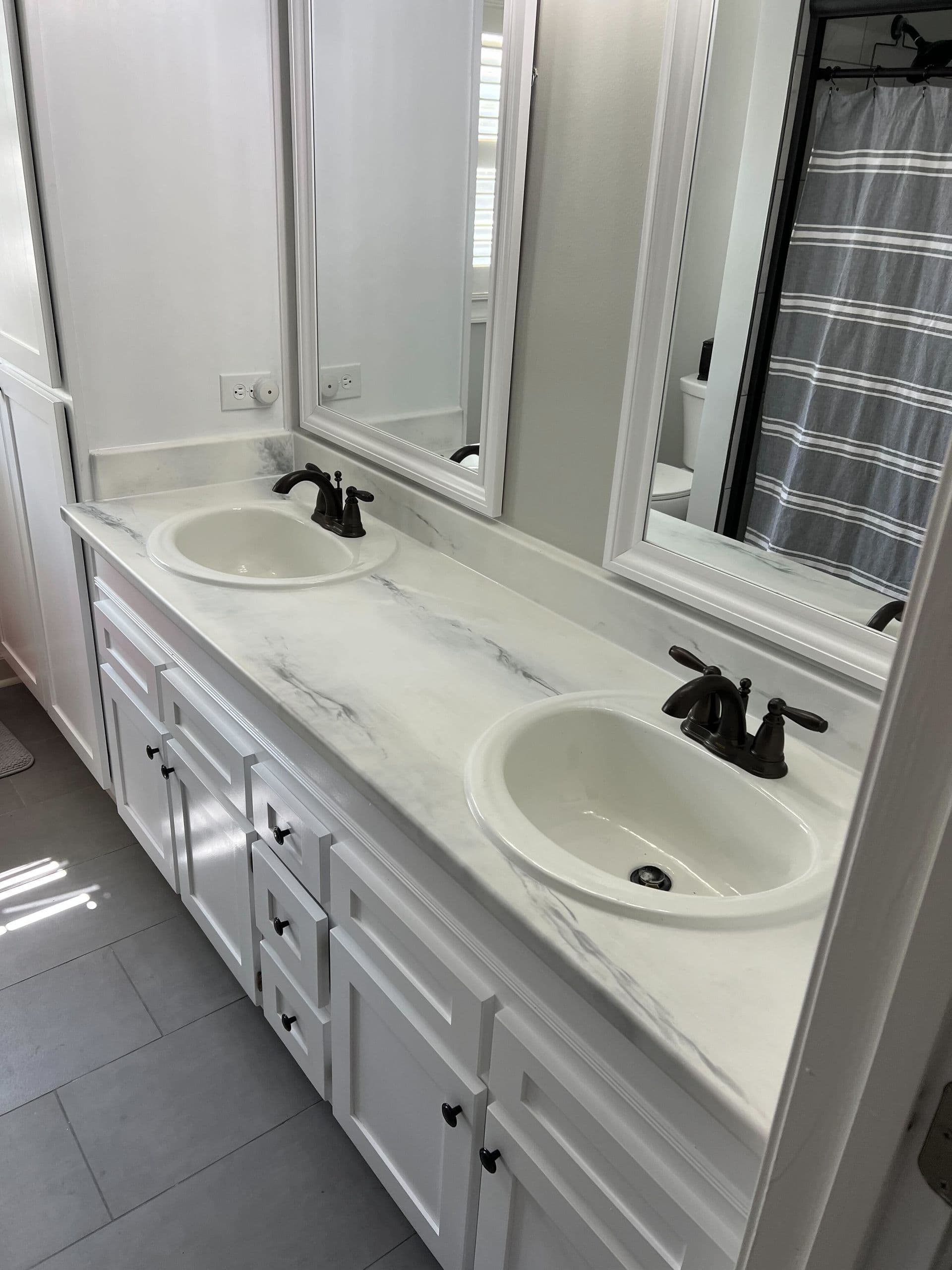 Modern bathroom with a dual-sink vanity featuring marble countertops, black faucets, and white cabinets. Mirrors above reflect natural light.