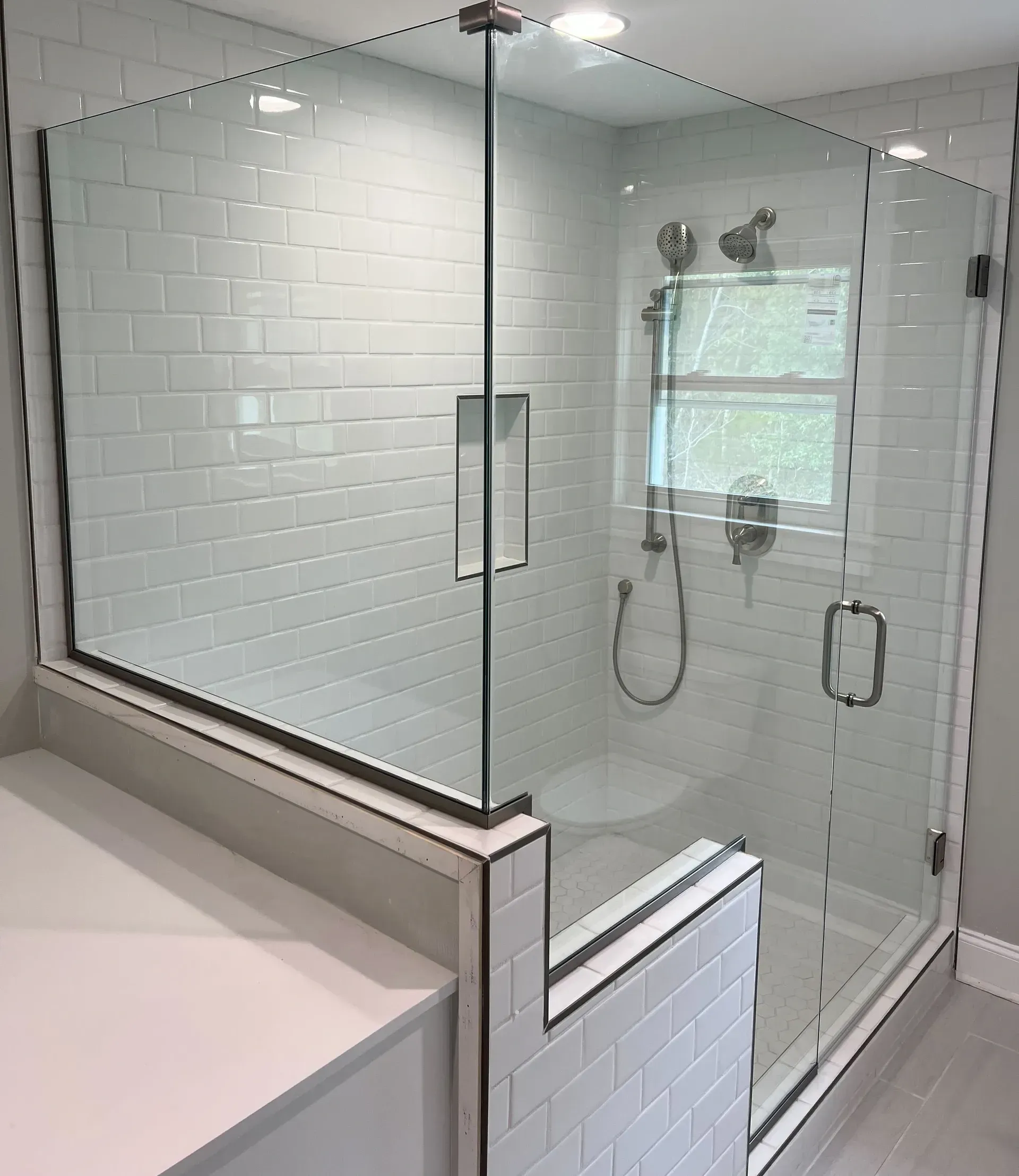 A modern bathroom with a glass-enclosed shower, white subway tile walls, dual shower heads, and a built-in shelf, creating a sleek, clean look.