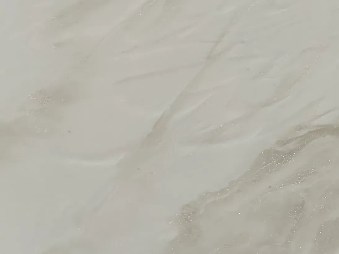 Creamy, smooth marble surface with subtle beige veining running diagonally. Light catches on the glossy finish, giving a clean, elegant feel.