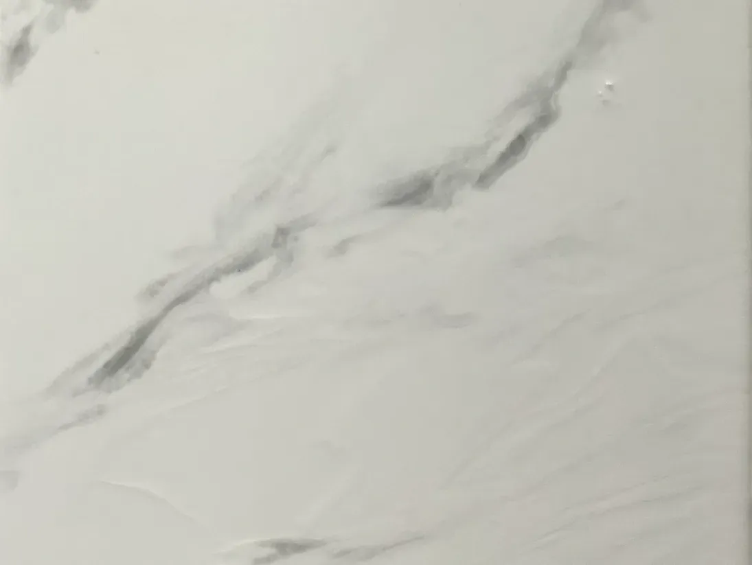 Close-up of a smooth white marble surface with soft gray veining patterns. The texture and tones create a calm, elegant ambiance.
